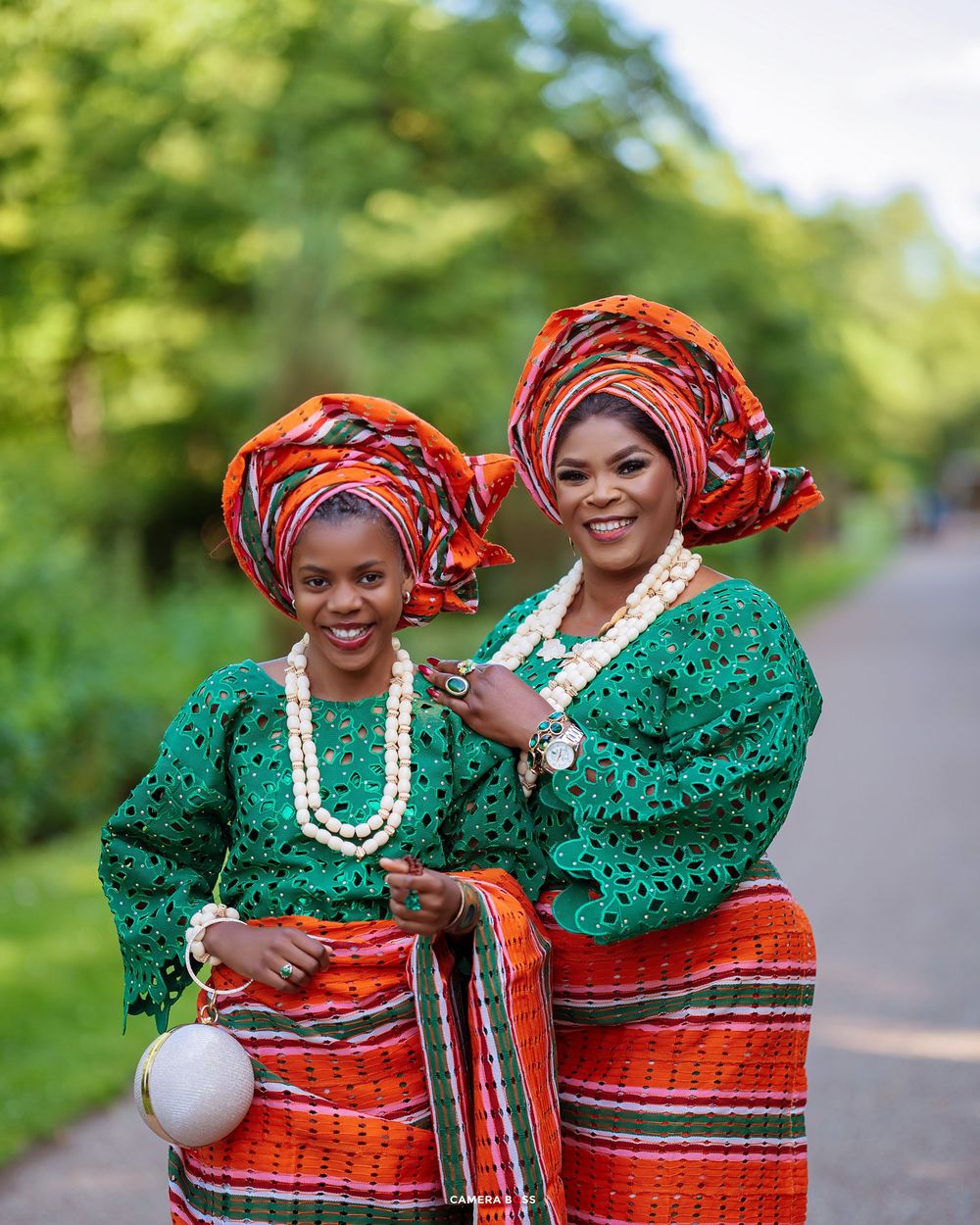Beautiful Nigerian traditional attire featuring emerald green lace tops and orange striped wrapper with gele headwraps and beaded necklaces.