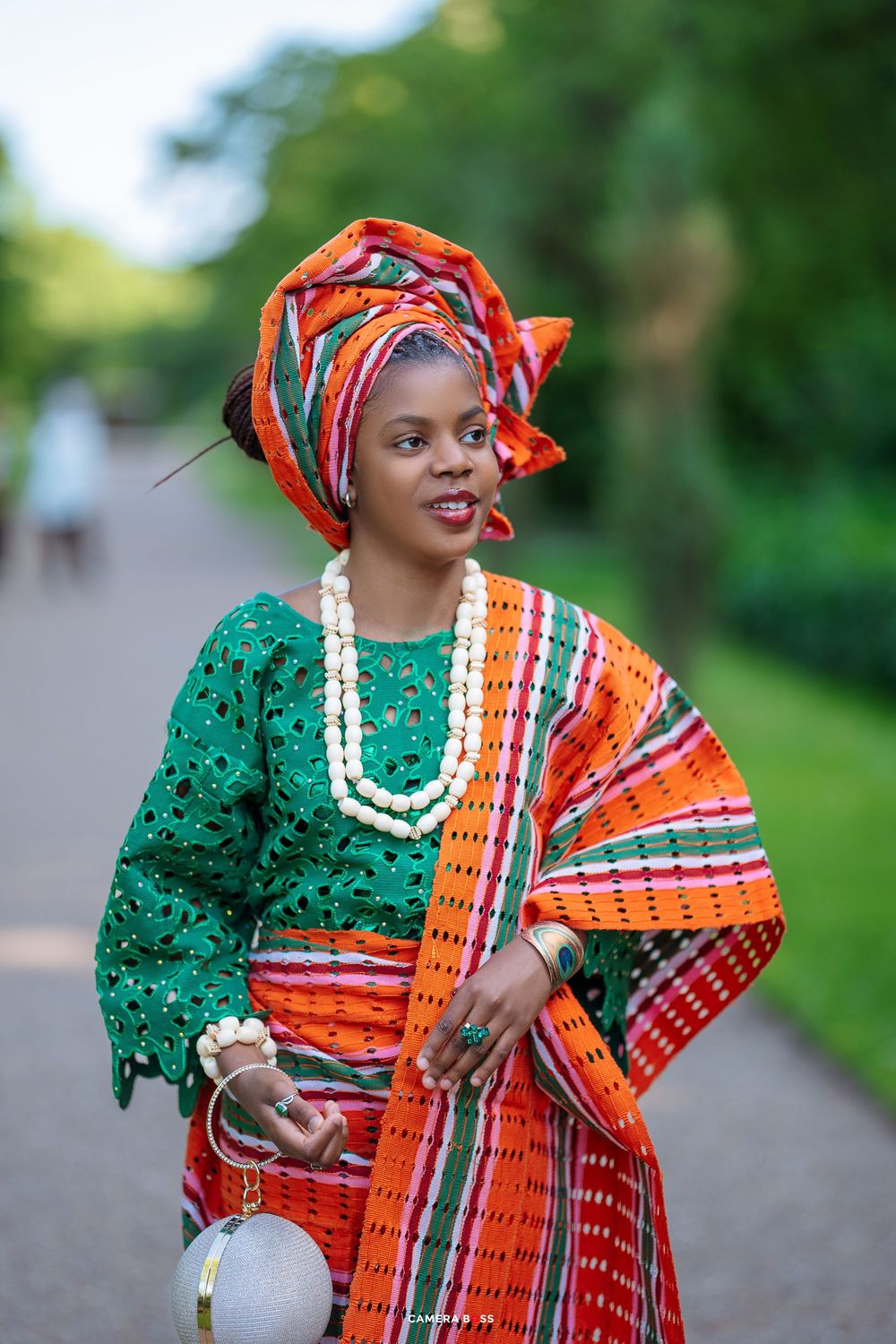 Traditional West African attire with emerald green top, orange striped wrapper, beaded necklace and elegant gele headwrap.