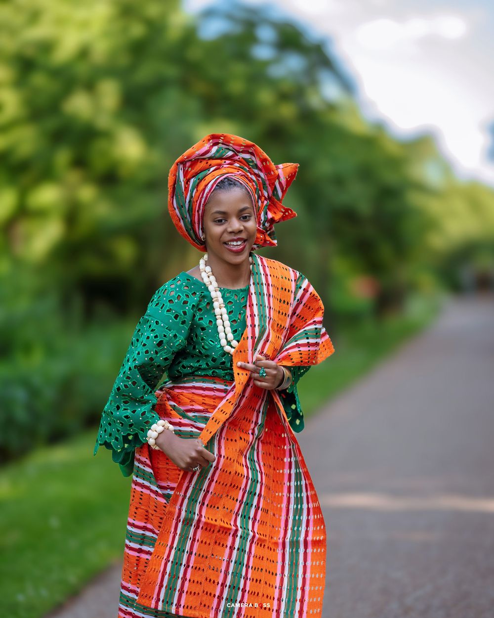 Beautiful African fashion on display with green lace blouse, orange striped wrapper and matching gele headwrap.