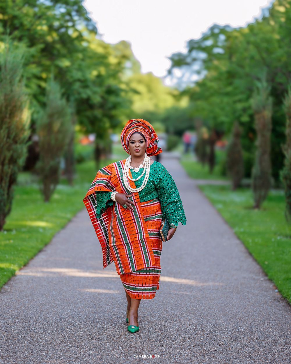 Colorful African dress with red plaid pattern and green accents shown on a tree-lined pathway.