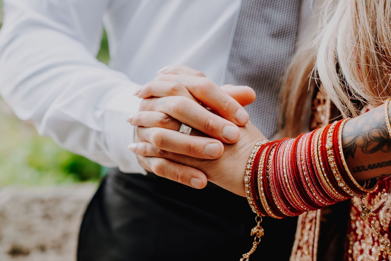 Close-up of two hands holding together, one with a tattoo and an engagement ring.