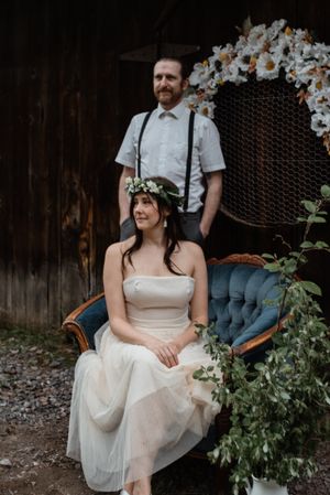 Rustic wedding portrait with vintage blue couch and floral backdrop against wooden barn wall.