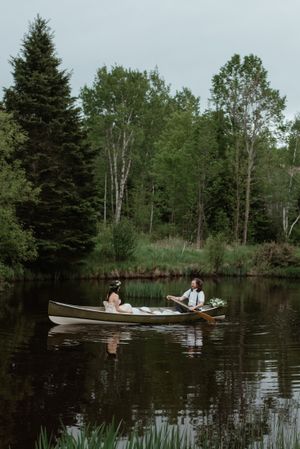 Couple paddling in a canoe on a tranquil lake surrounded by evergreen trees.