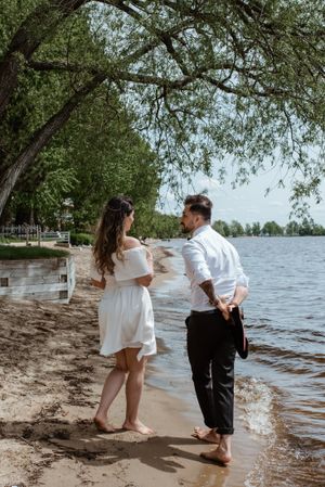 Couple in white and black attire sharing playful moment on lakeside beach.
