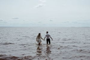 Two people holding hands while wading through calm ocean waters.