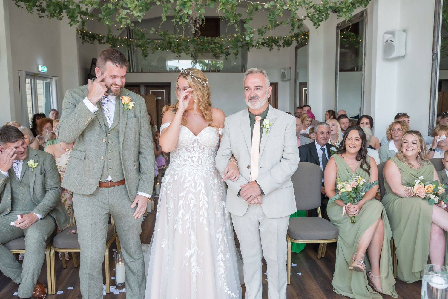 Wedding attendees in sage green and white attire share an emotional moment during indoor ceremony.