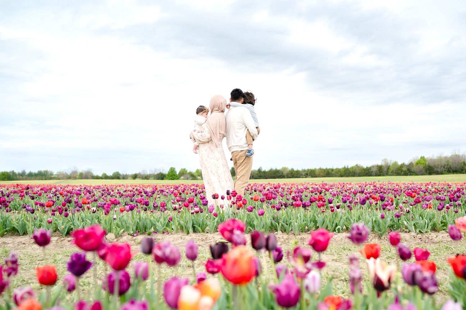 A couple stands together in a vibrant field of colorful blooming tulips against a cloudy sky in springtime.