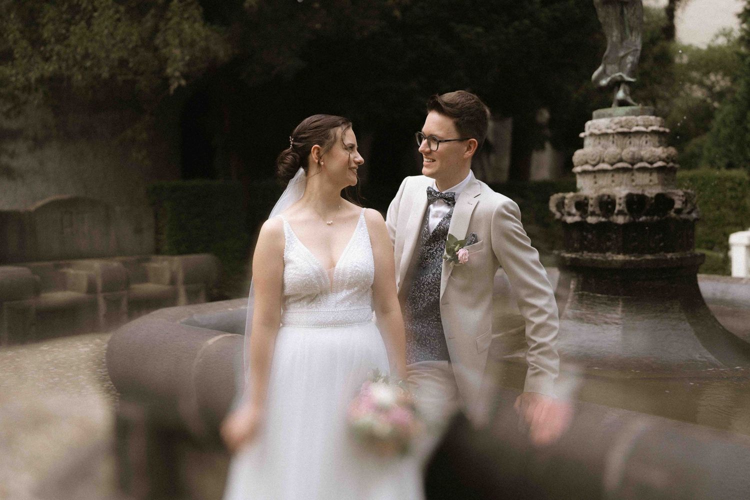 A couple shares a joyful moment in their wedding attire near classic stone architecture.