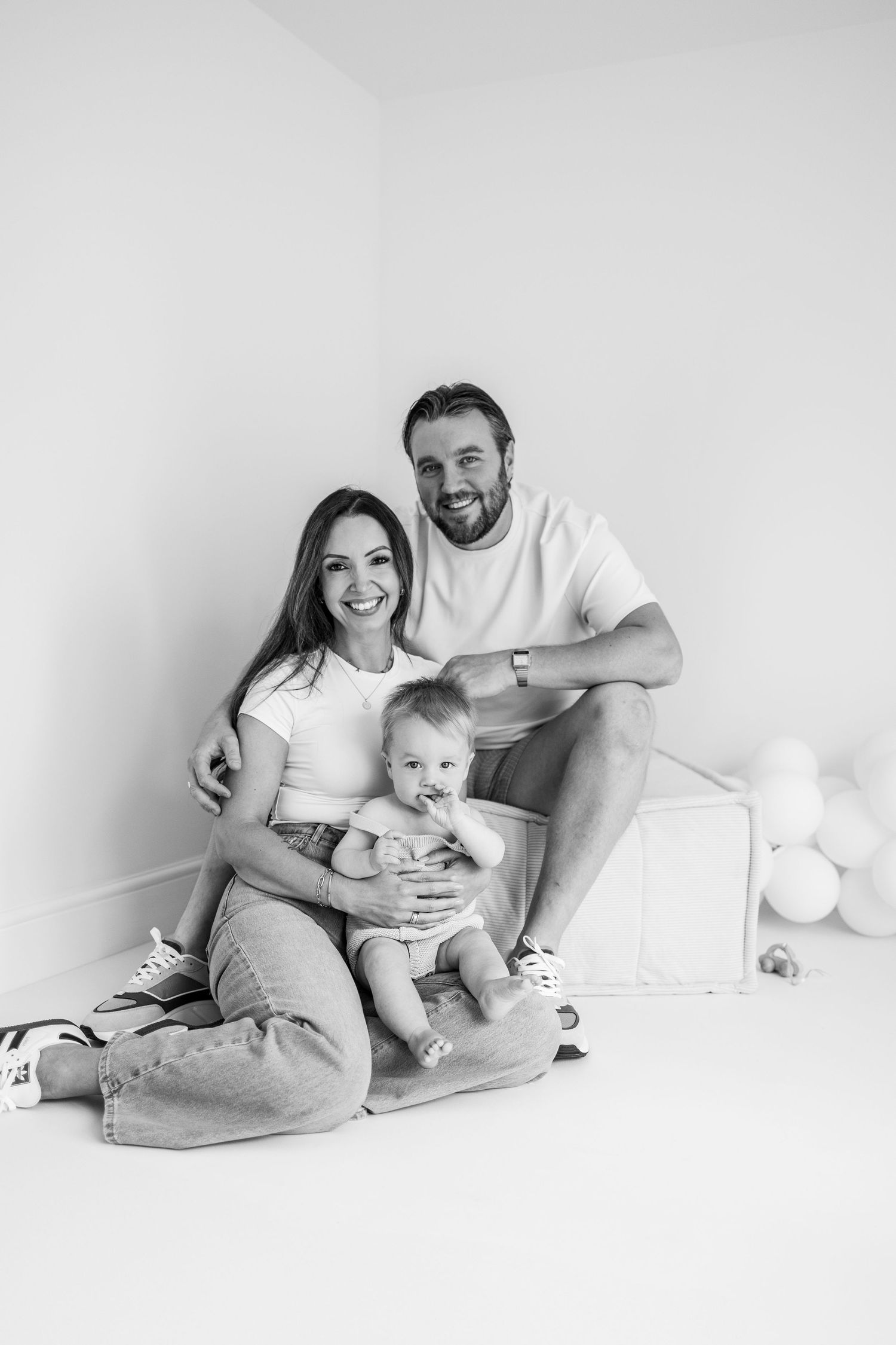 A family sits together in a bright white room for a casual portrait session.