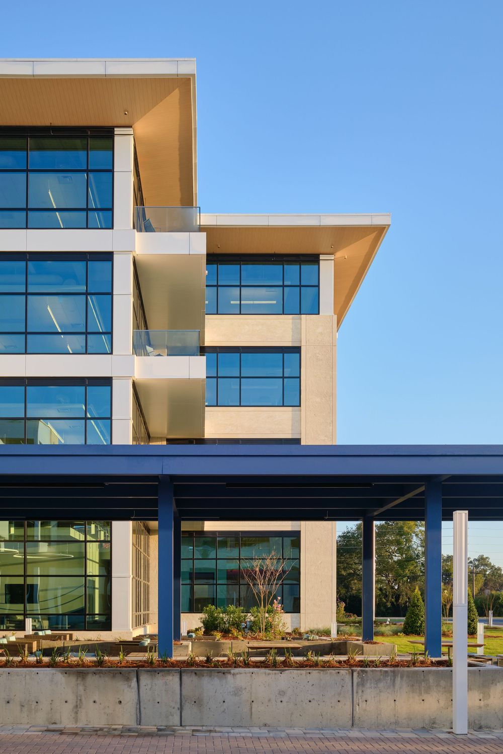 Modern office building exterior featuring beige tiers with glass windows and a covered entrance area against blue sky.