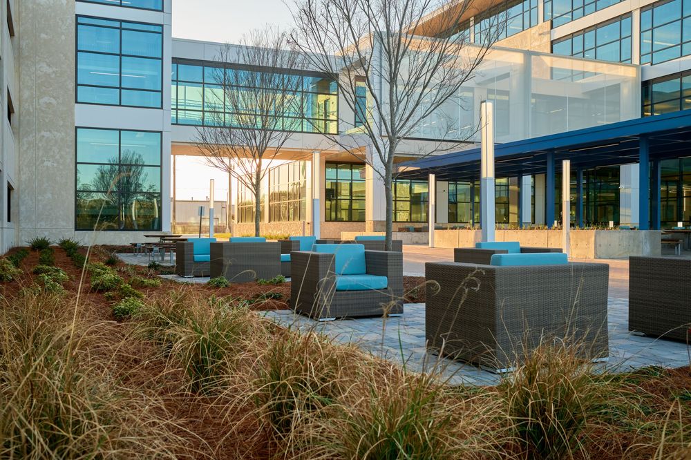 Modern office building courtyard with blue outdoor furniture and ornamental grasses during daytime.