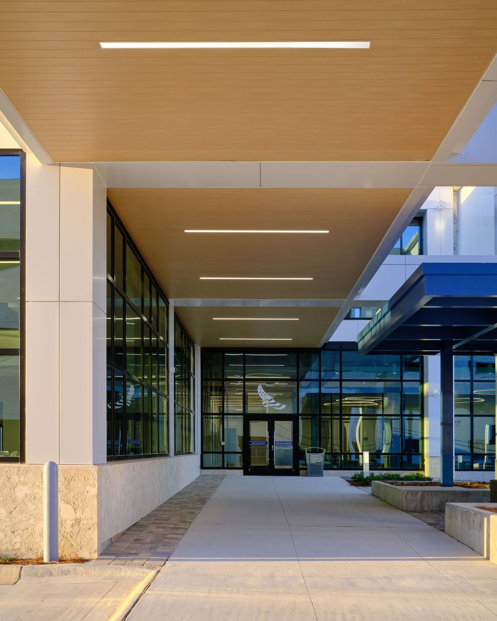 Covered entrance walkway of a commercial building with white columns and linear lighting fixtures on the ceiling.
