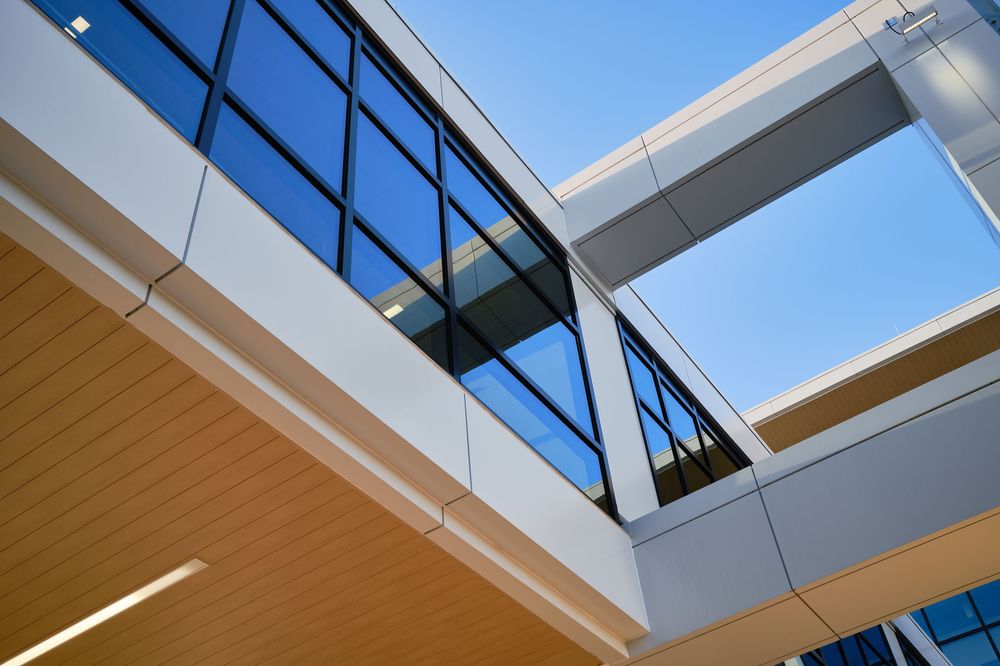 Angular architectural detail of modern building featuring glass windows, white panels, and wooden ceiling with lighting.