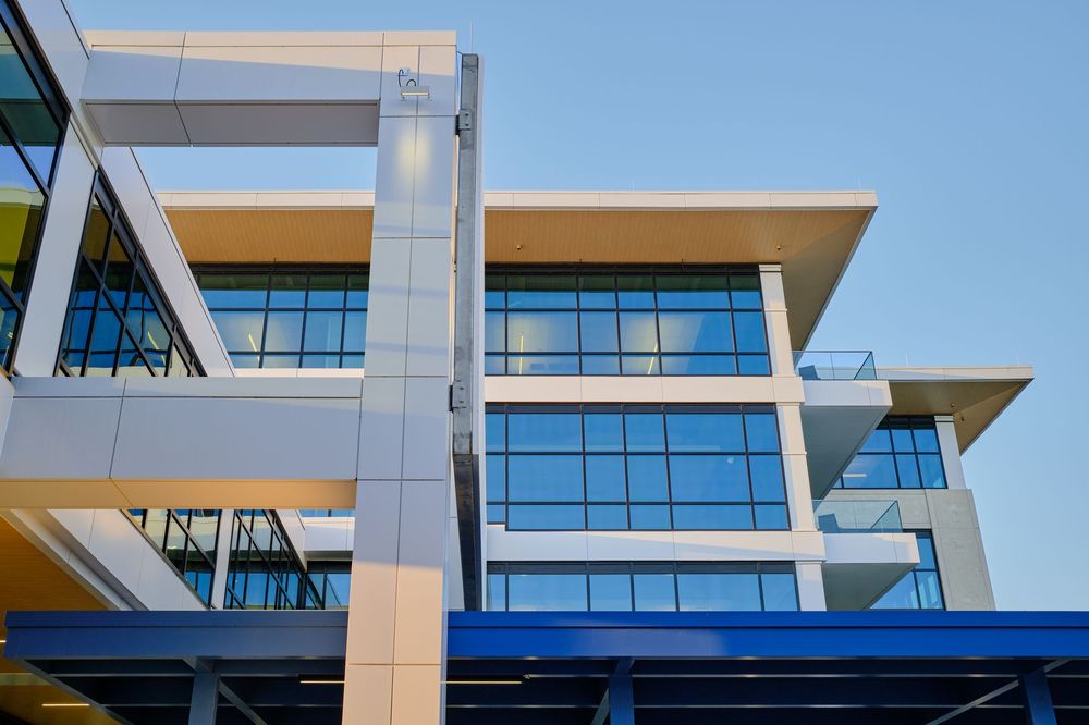 Modern office building exterior featuring angular architecture with glass windows and metallic accents against blue sky.