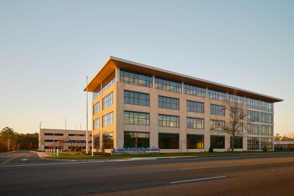 Modern office building exterior with orange accents and glass windows in a commercial business park at sunset.