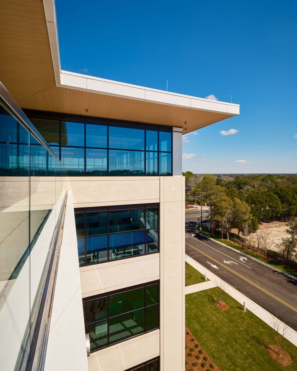 Modern office building exterior with angular architecture, glass windows, and limestone facade against bright blue sky.