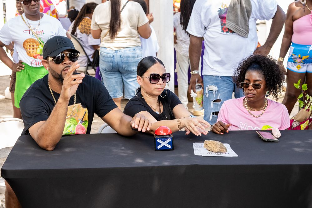 People seated at tables during a community meet and greet event with palm trees visible in background.