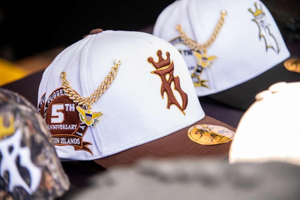 Collection of white baseball caps with embroidered brown logos arranged in a row against a dark background.