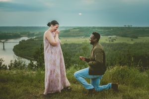 A romantic proposal moment on a hilltop overlooking a winding river during sunset.