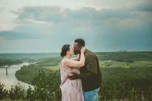 A romantic couple shares an intimate moment overlooking a winding river valley from a scenic hilltop viewpoint.