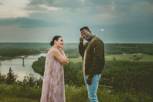 Two people share an emotional celebration moment on a scenic hilltop with a river view in the background.