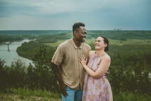 A couple shares a joyful moment while standing together on a scenic overlook with rolling hills in the background.
