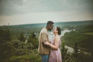 A romantic couple embraces on a hilltop overlooking a scenic river valley on a misty afternoon.
