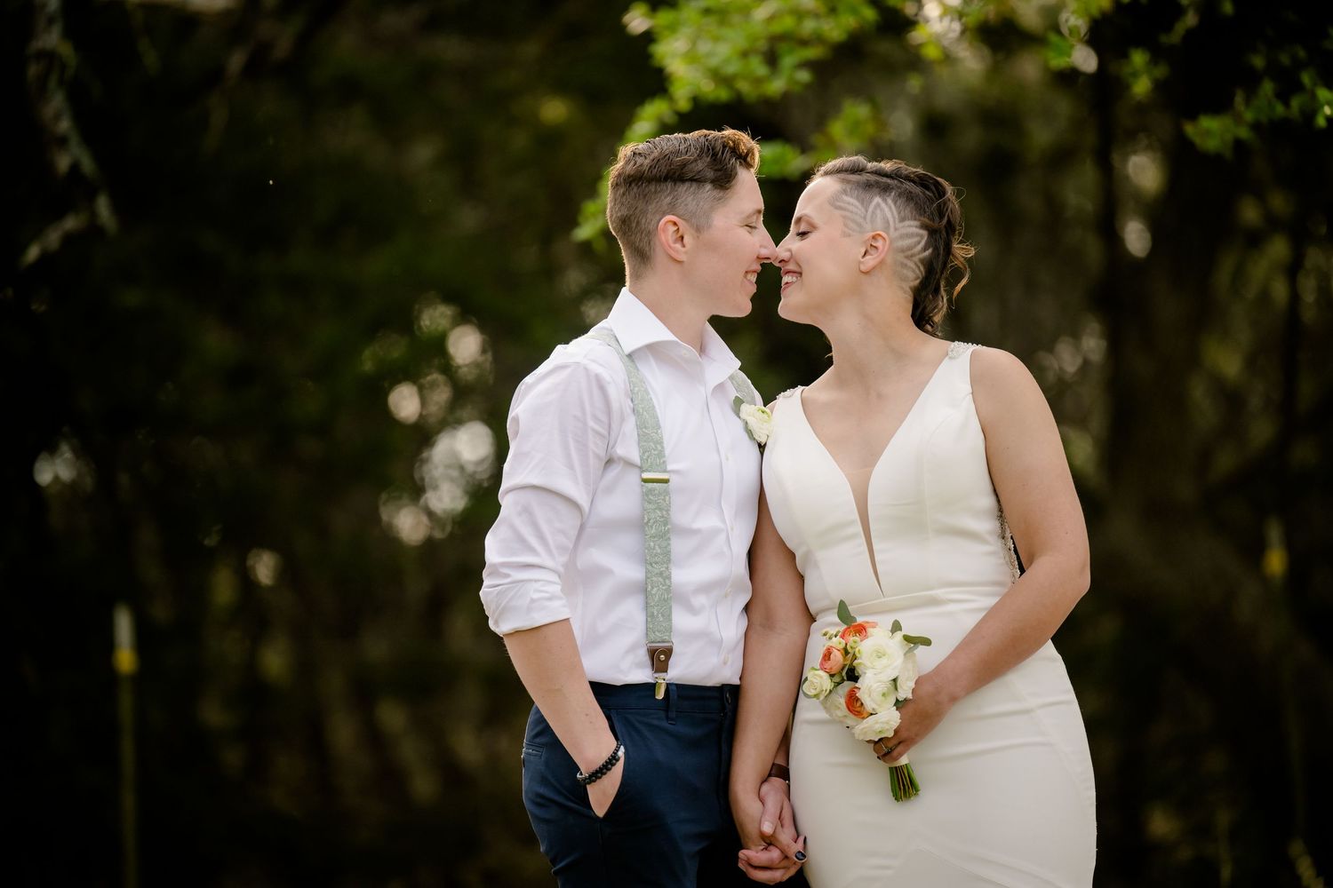 A romantic wedding couple embraces and kisses in a scenic outdoor garden setting with natural lighting.