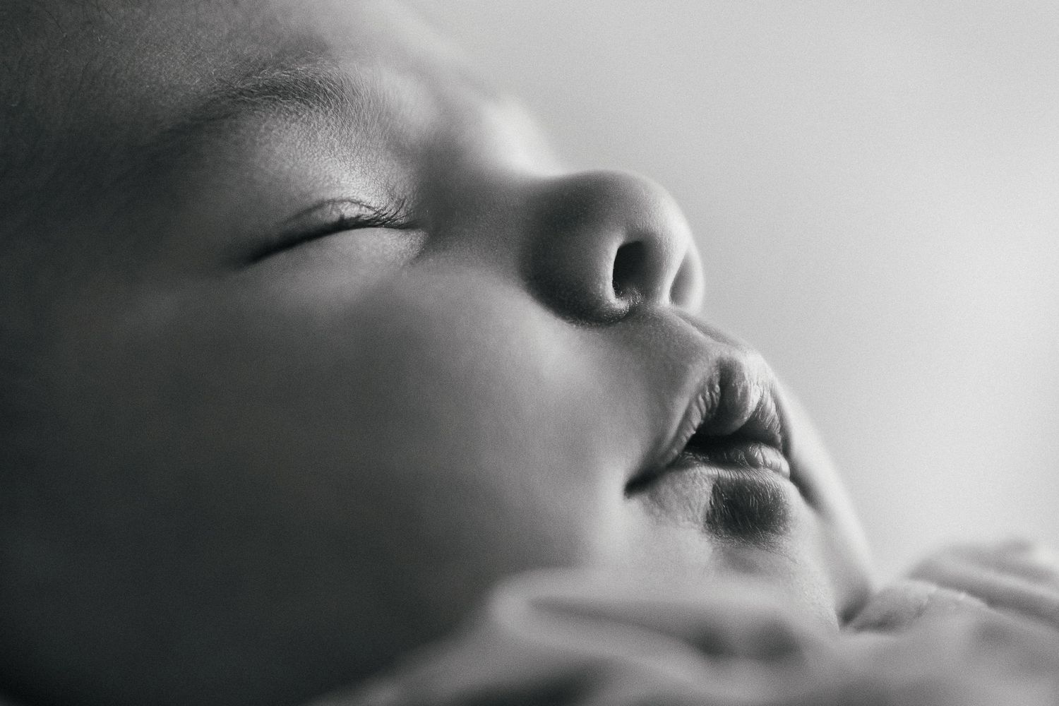 A sleeping newborn wrapped in a cream colored blanket is held gently in tattooed hands while resting peacefully.