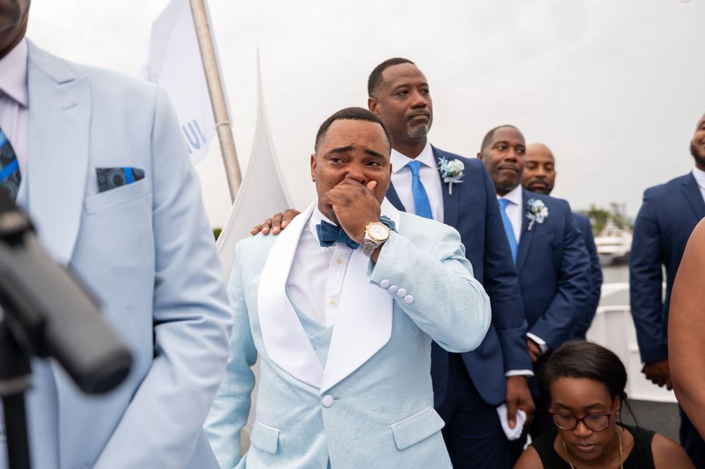 Groomsmen adjusting bow ties and jackets in candid yacht wedding photo