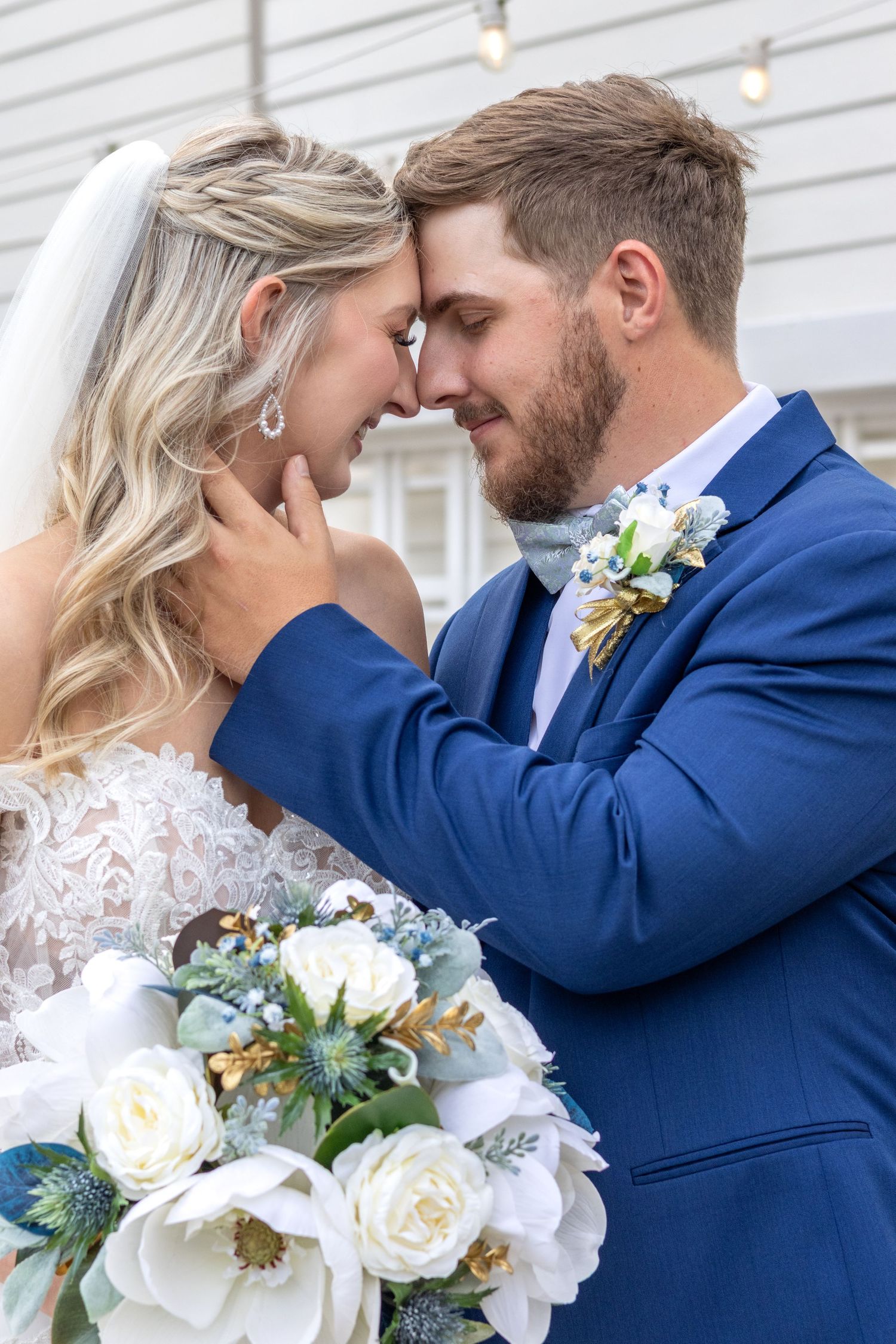 Newlywed couple shares intimate moment with floral bouquet against white backdrop.