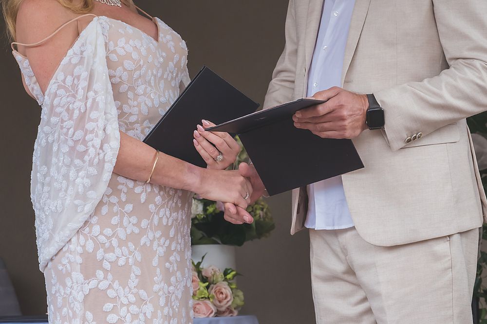 A couple exchanges vows during a wedding ceremony while holding a black book between them.