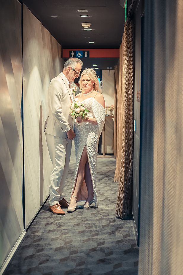 A couple shares a tender moment in a hallway, with the bride wearing a lace gown and holding a small bouquet.