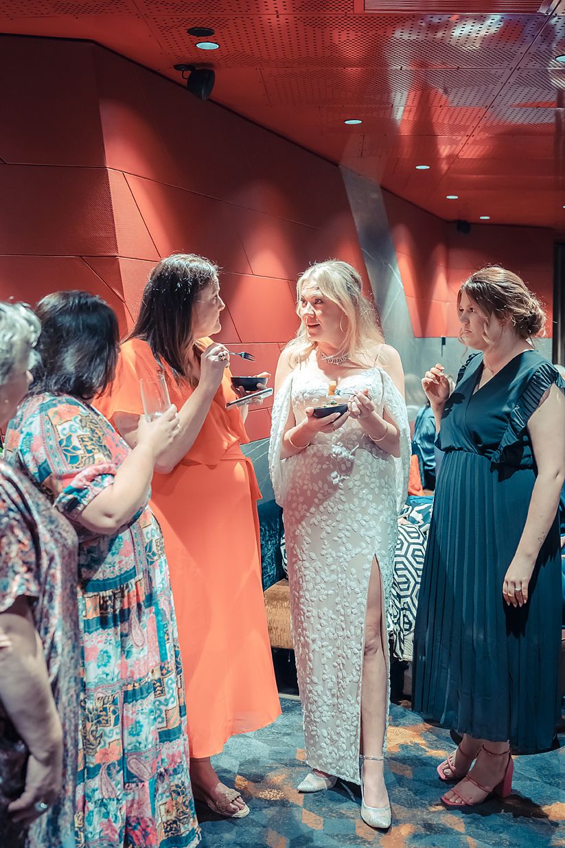 A group of friends in elegant attire gather at a social event with red walls and modern lighting.