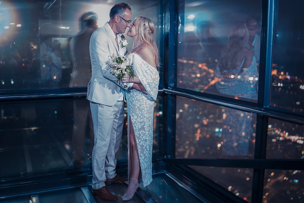 A couple shares a romantic moment in a high-rise building at night with city lights glowing through the windows.