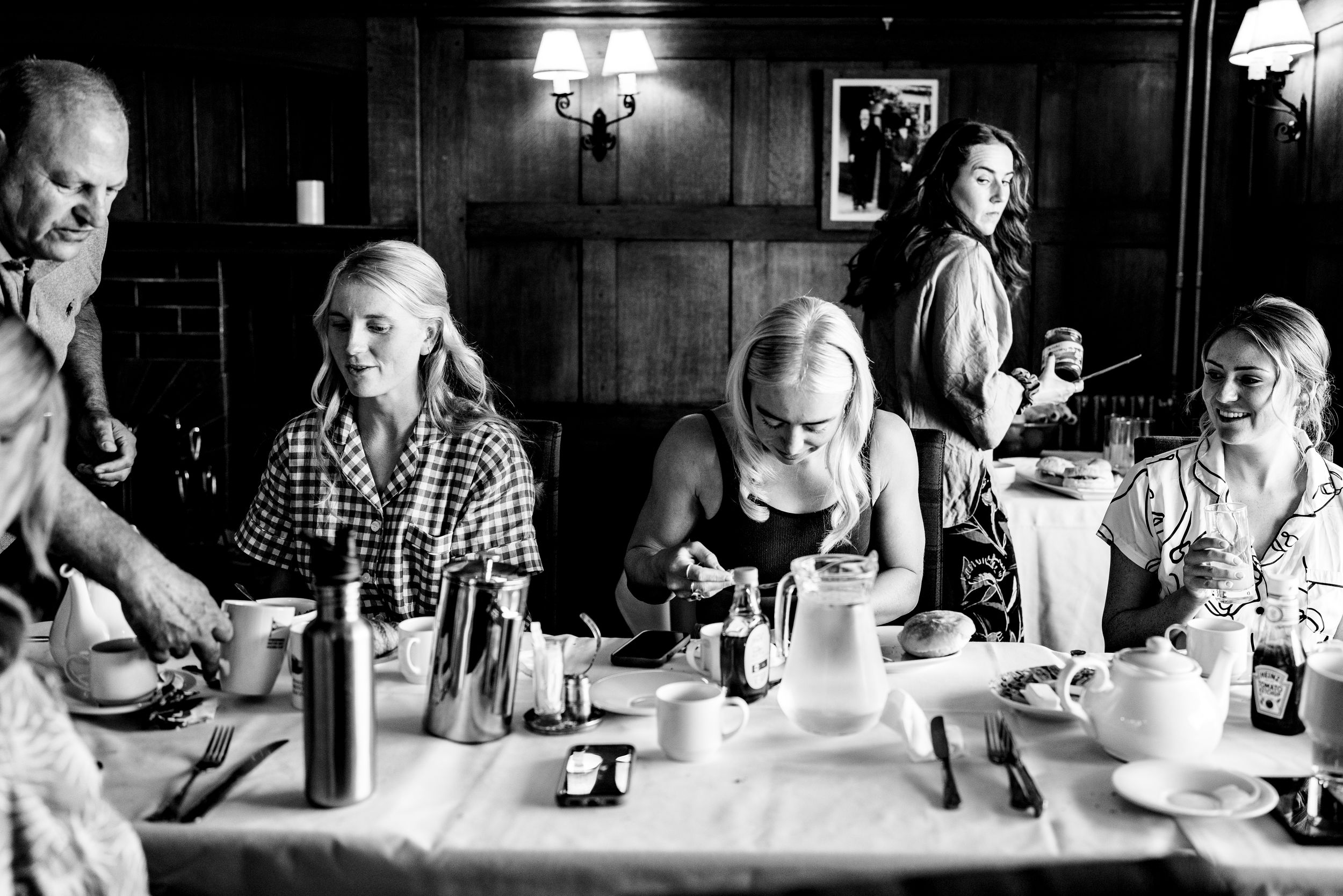 Black and white photo of women gathered around a dining table at a wedding breakfast in a classic restaurant.