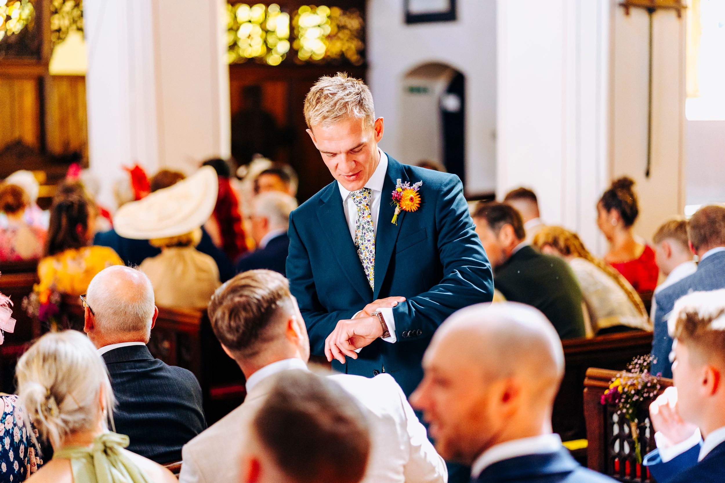 Groom in navy suit checking his watch while waiting at the church altar before the ceremony.