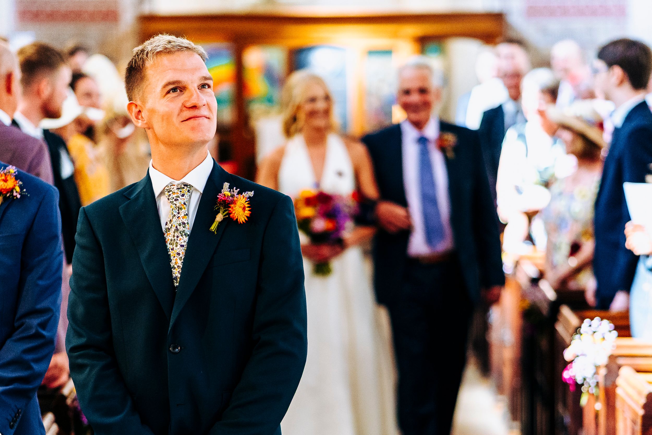 Emotional groom smiling as he watches his bride walk down the church aisle toward him.