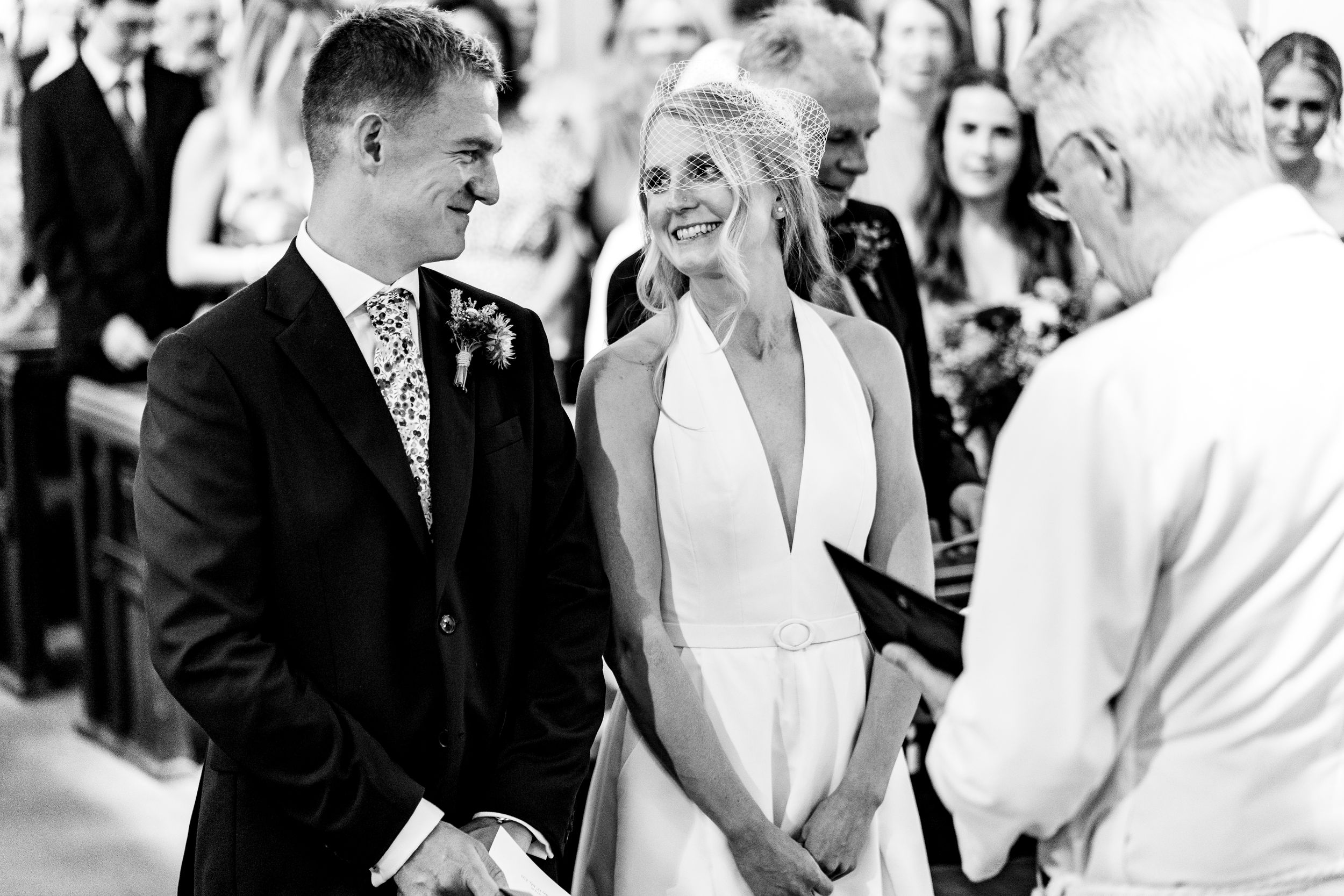 Black and white photo of bride and groom smiling at each other during their church ceremony.