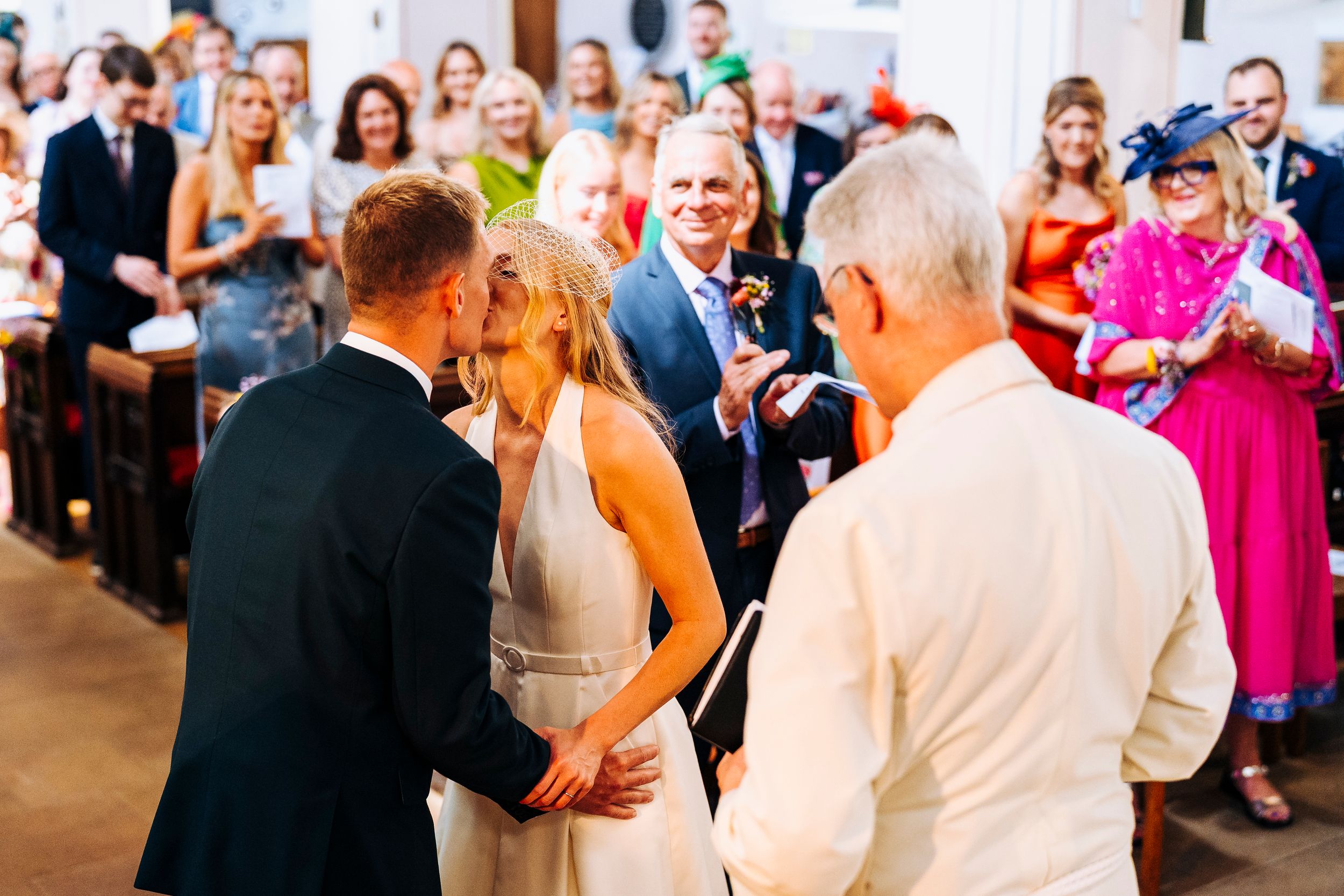 Bride and groom sharing their first kiss at the altar surrounded by joyful wedding guests.