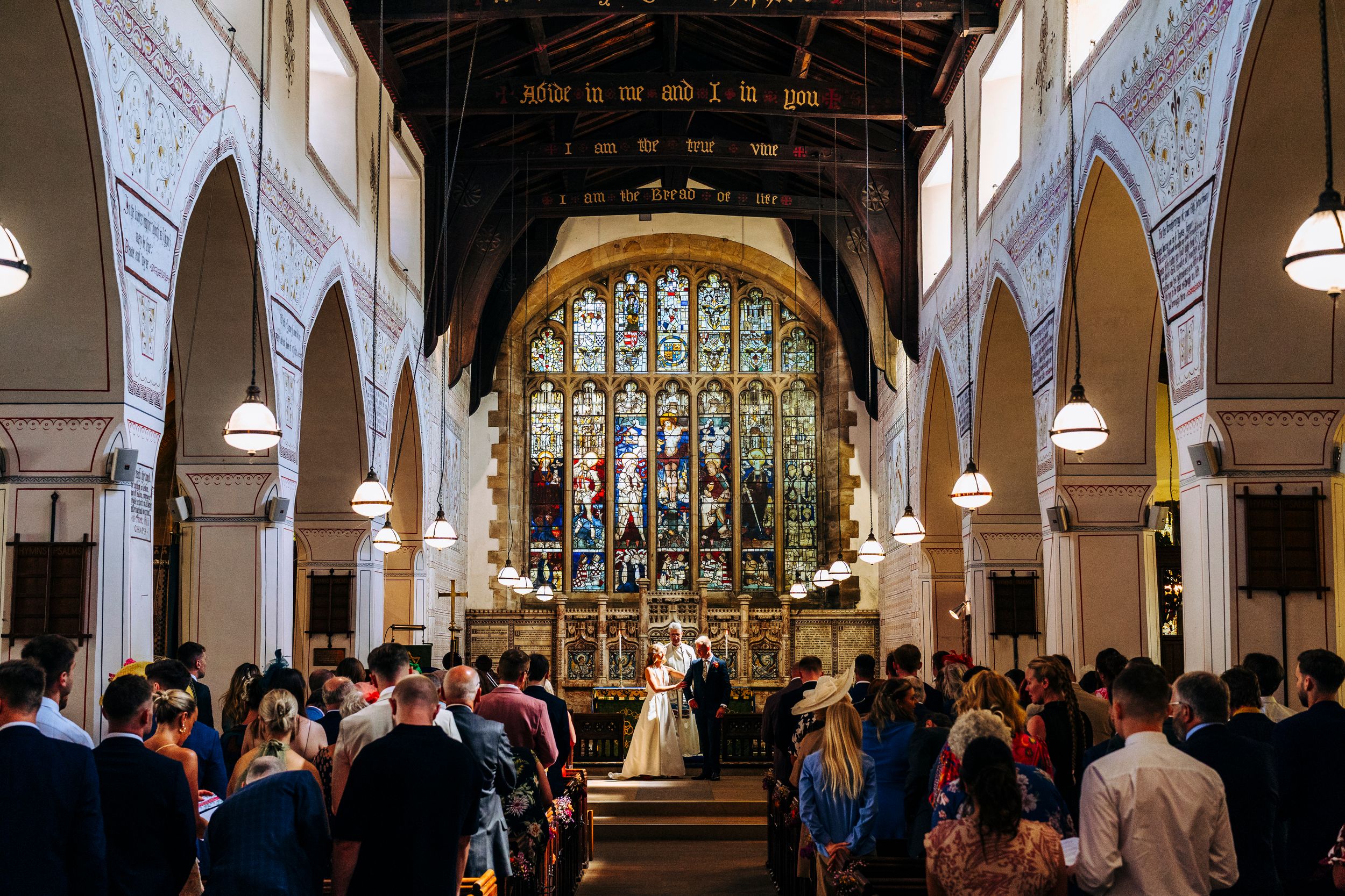 Wedding ceremony inside historic church with stained glass window and guests filling wooden pews.