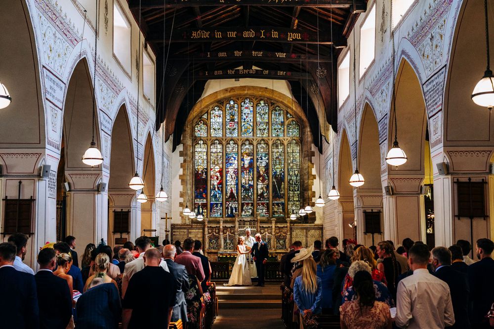 Wedding ceremony inside historic church with stained glass window and guests filling wooden pews.