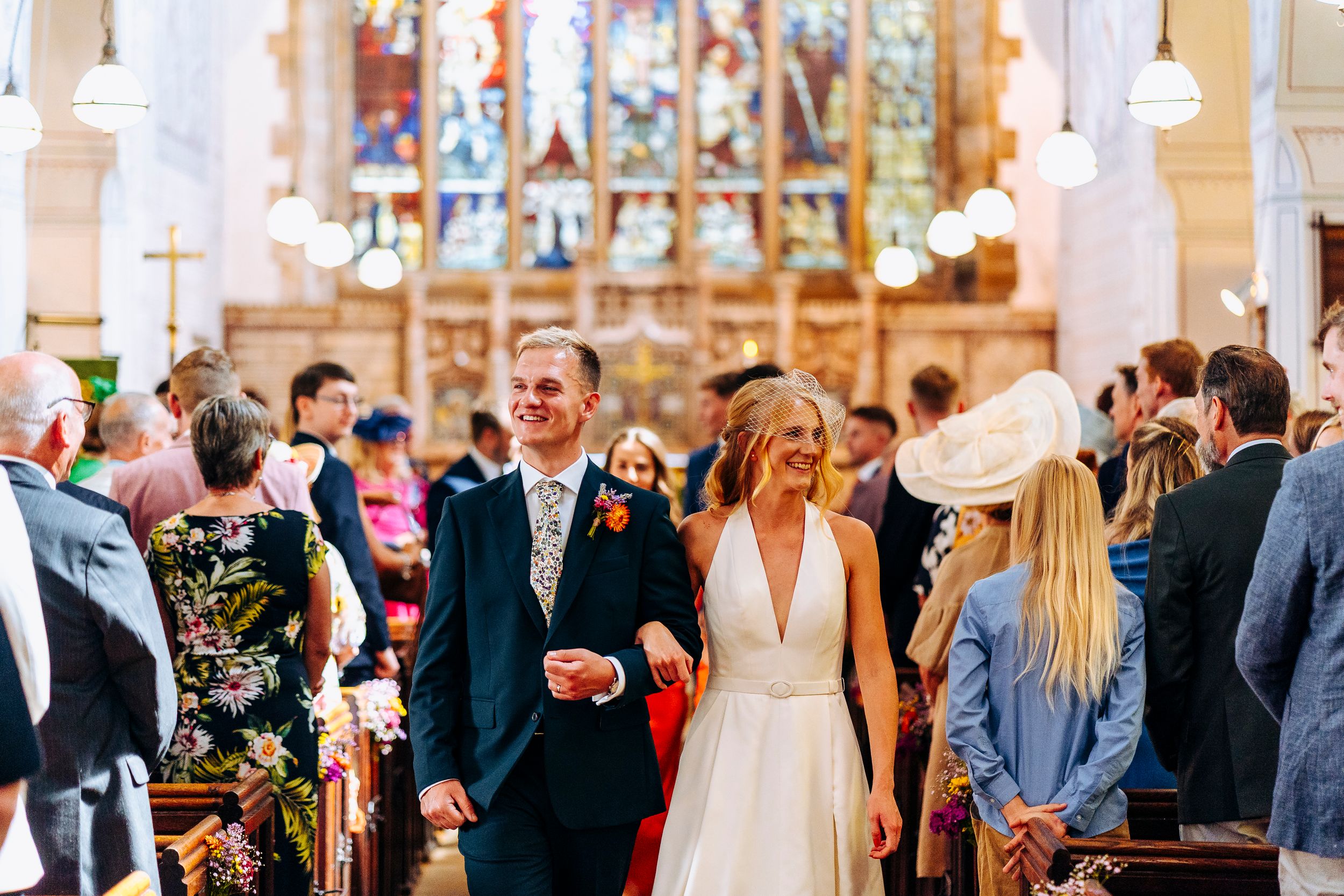 Bride and groom walk hand in hand down church aisle after wedding ceremony with guests watching.