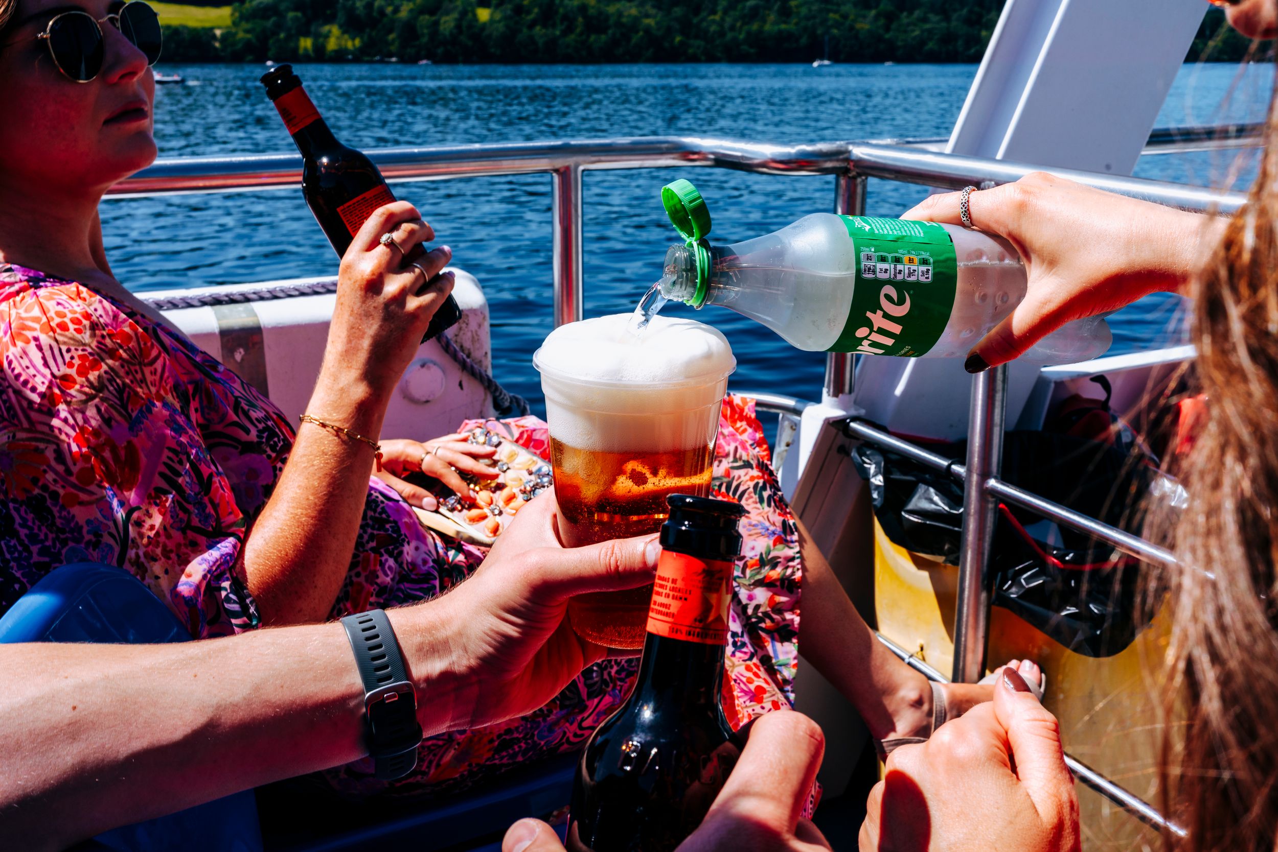 Friends toasting with beer bottles and glasses on a sunny boat trip on the water.