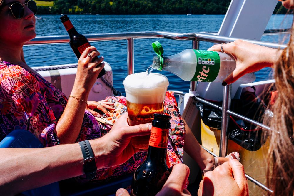 Friends toasting with beer bottles and glasses on a sunny boat trip on the water.