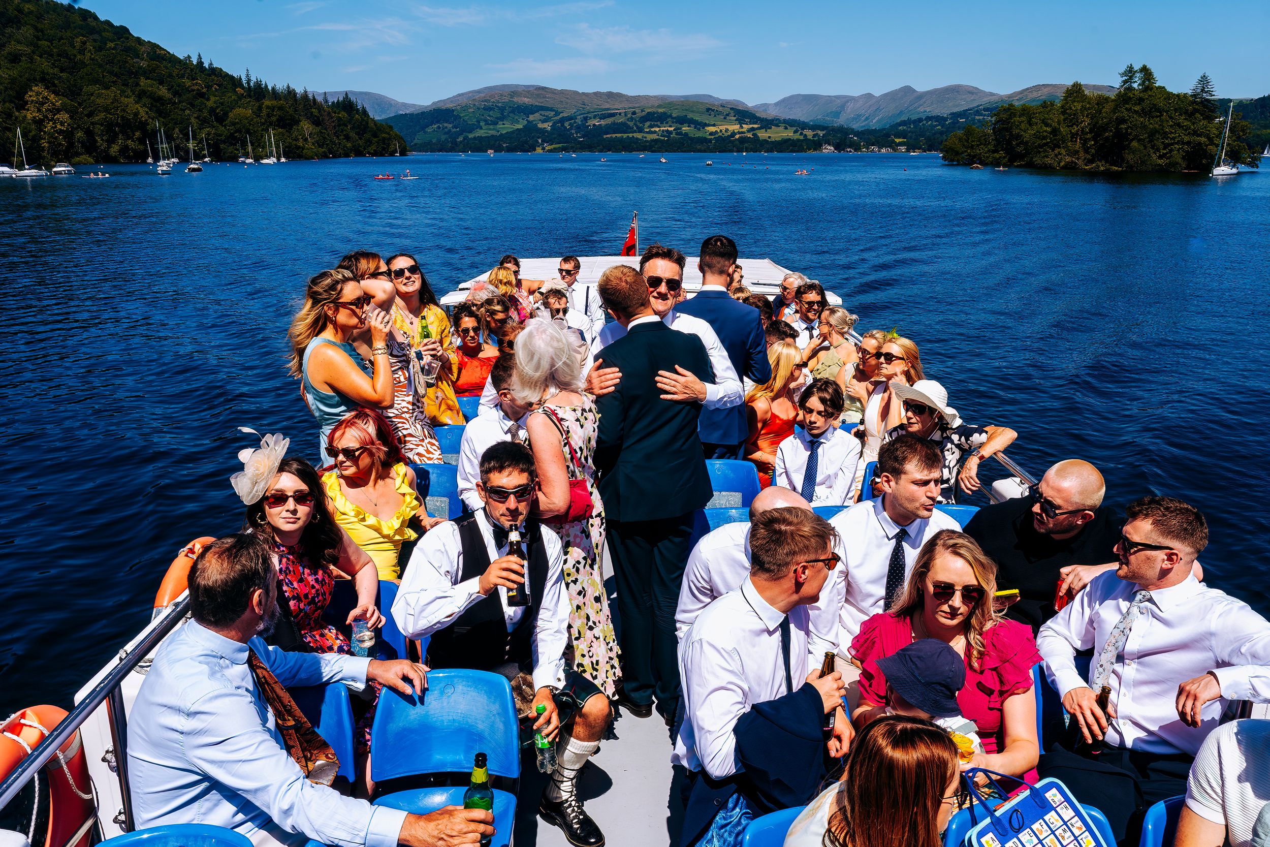 Large wedding party celebrating on a boat cruise across a beautiful scenic lake.
