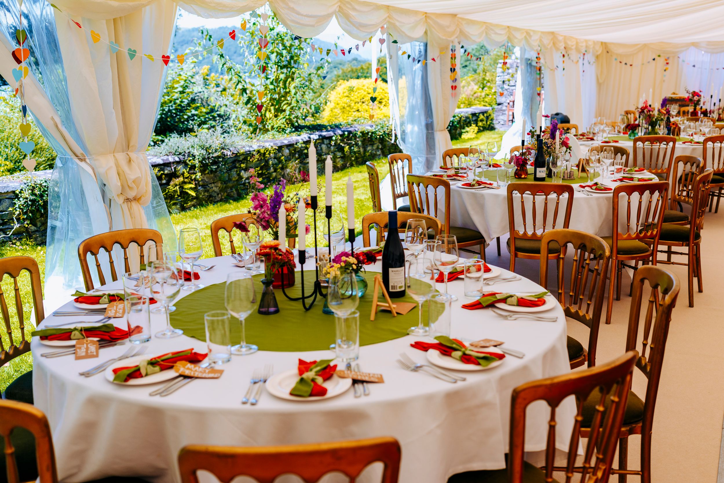 Elegant wedding reception marquee with round tables, floral centerpieces, and colorful bunting.