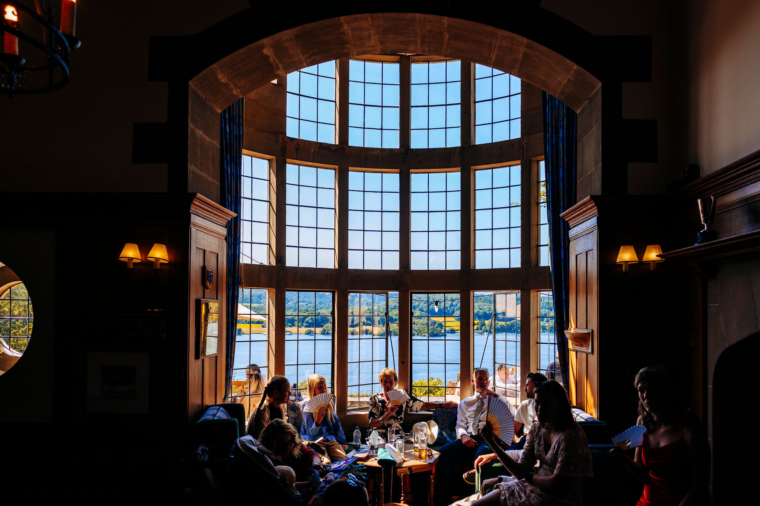 Wedding guests dining in a grand room with large windows overlooking a scenic lake.