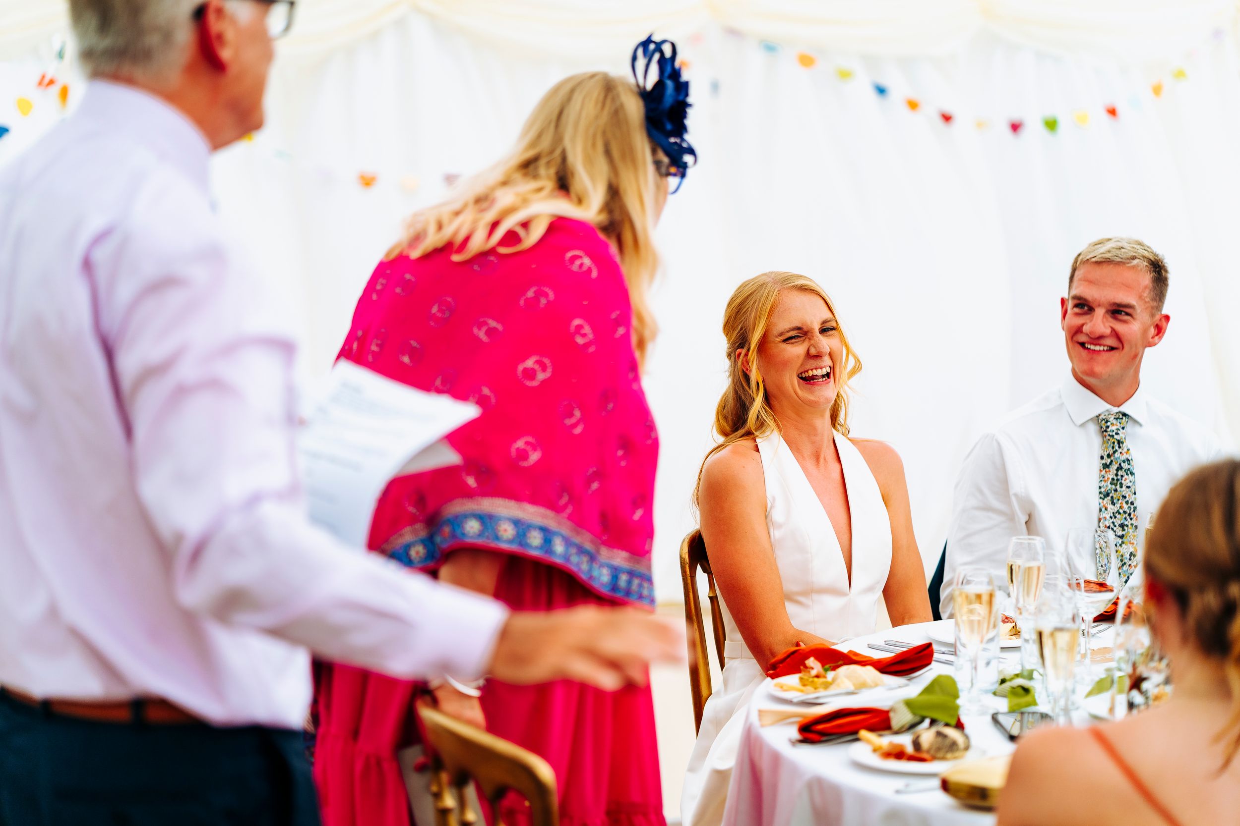 A laughing bride in a white dress enjoys a joyful moment with guests during the wedding reception.