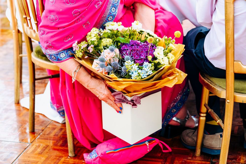 A wedding guest in a pink sari holds a beautiful bouquet of purple and yellow flowers.